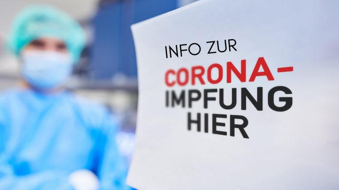 Frau mit Schutzanzug und Maske, Text: Info zur Corona-Impfung hier, Credit: Canva