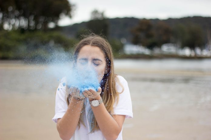 junge Frau bläst in blauen Staub, Credit: Joel Henry, Unsplash