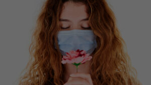 junge Frau mit roten Haaren und Mund-Nasenschutz riecht an Blume, Credit: engin akyurt, Unsplash