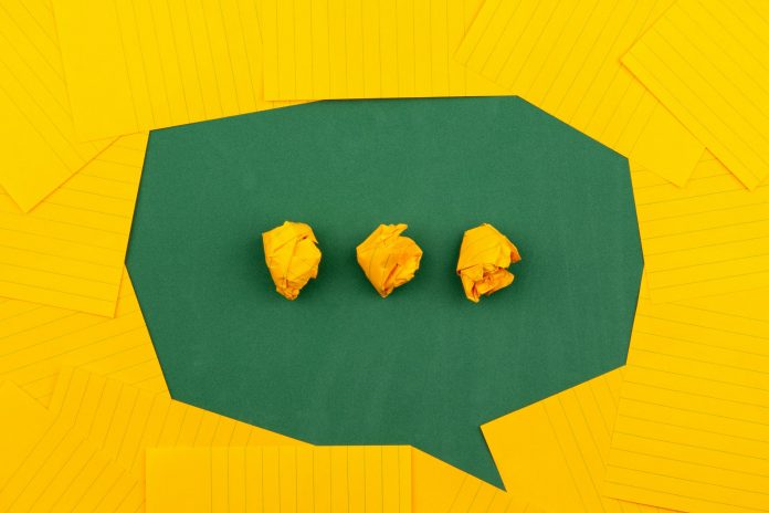 orangefarbene Blätter liegen auf einer grünen Tafel und bilden mit drei zerknitterten Papieren eine Chatblase. Foto: Volodymyr Hryshchenk, Unsplash